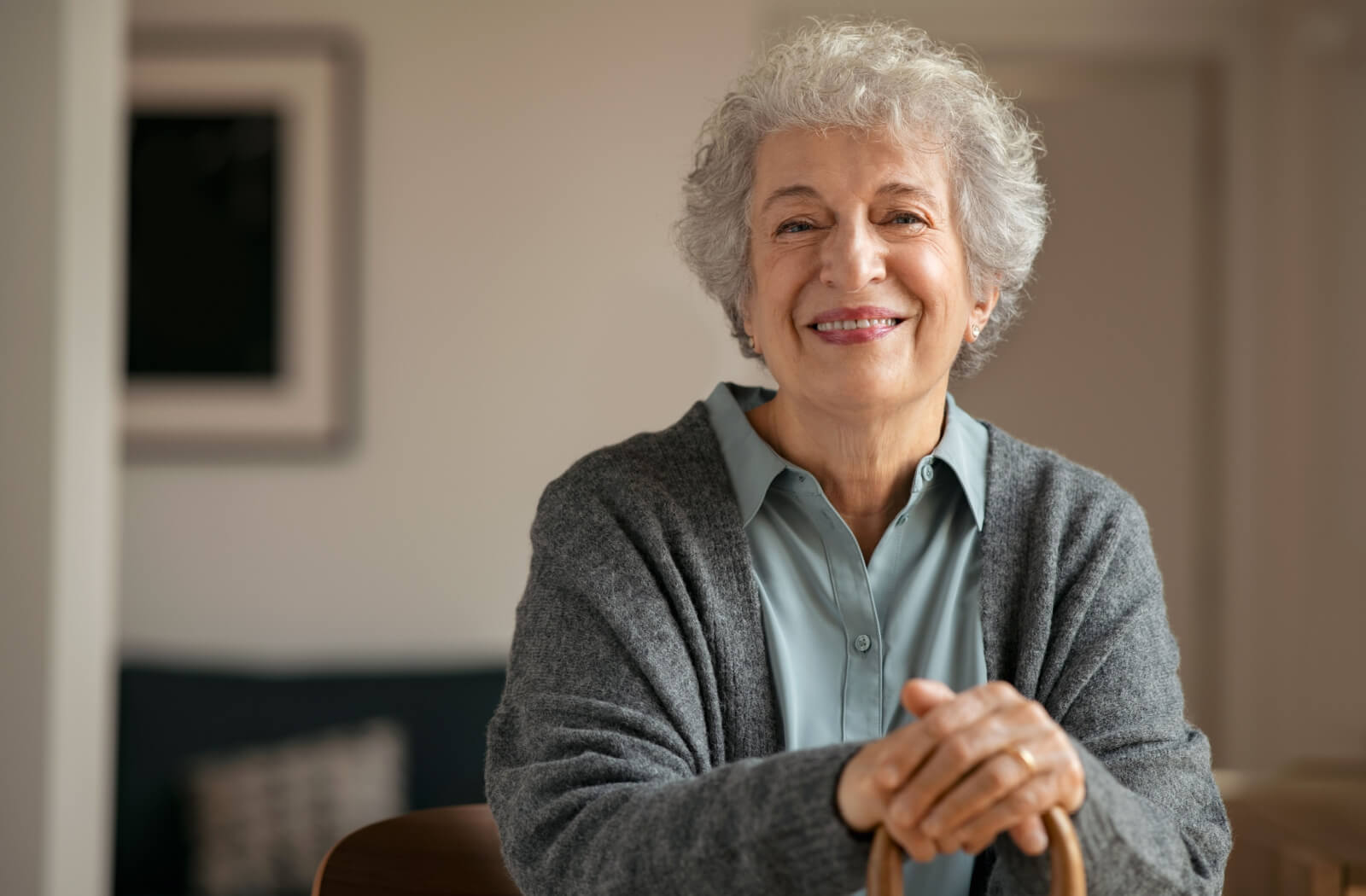 A senior woman with short gray hair holding a cane smiling and looking directly in the camera.
