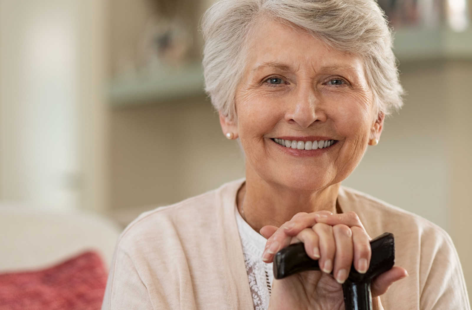 A senior woman smiling with short gray hair, holding a cane and looking directly at the camera.