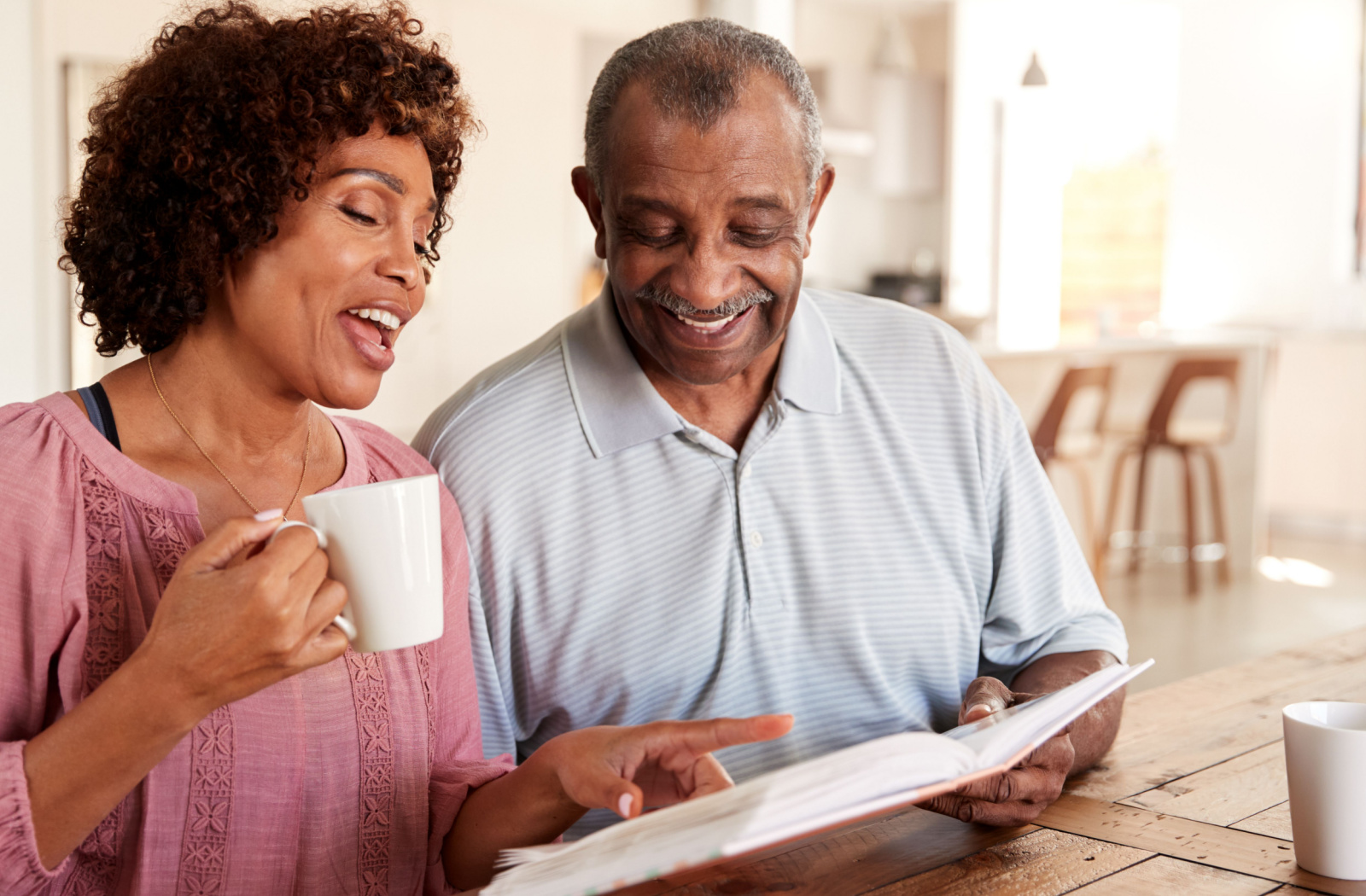 A senior man and his daughter, smiling and looking through photo album together at home.