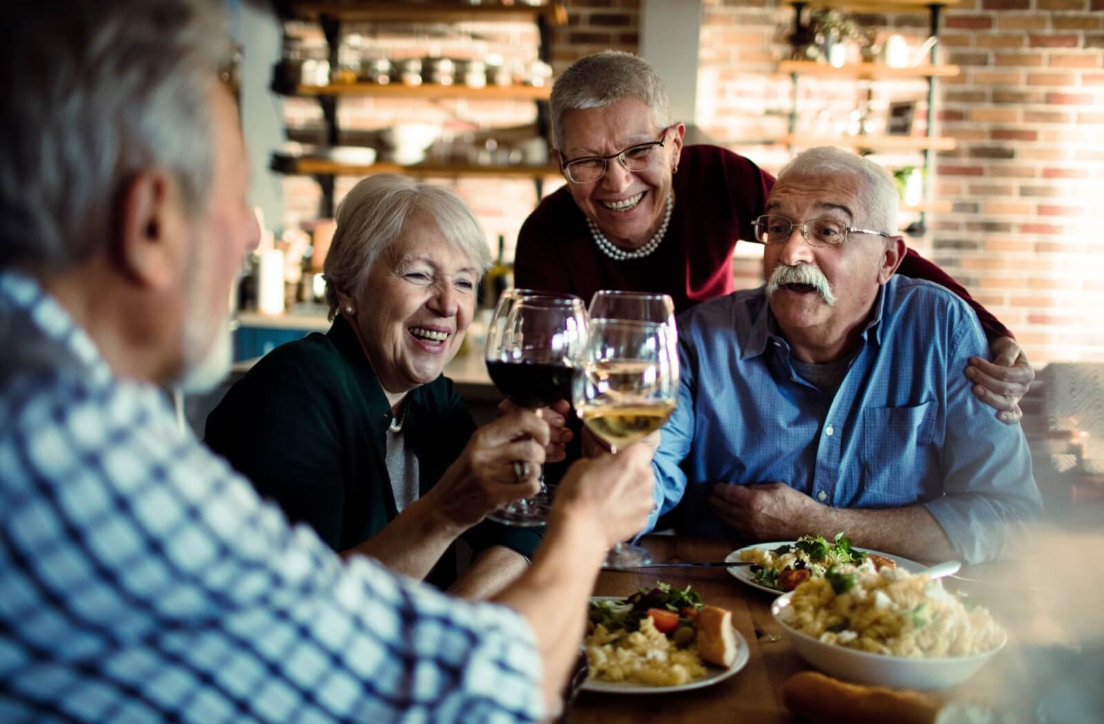 A happy group of seniors clink their wine glasses over a delicious shared meal.