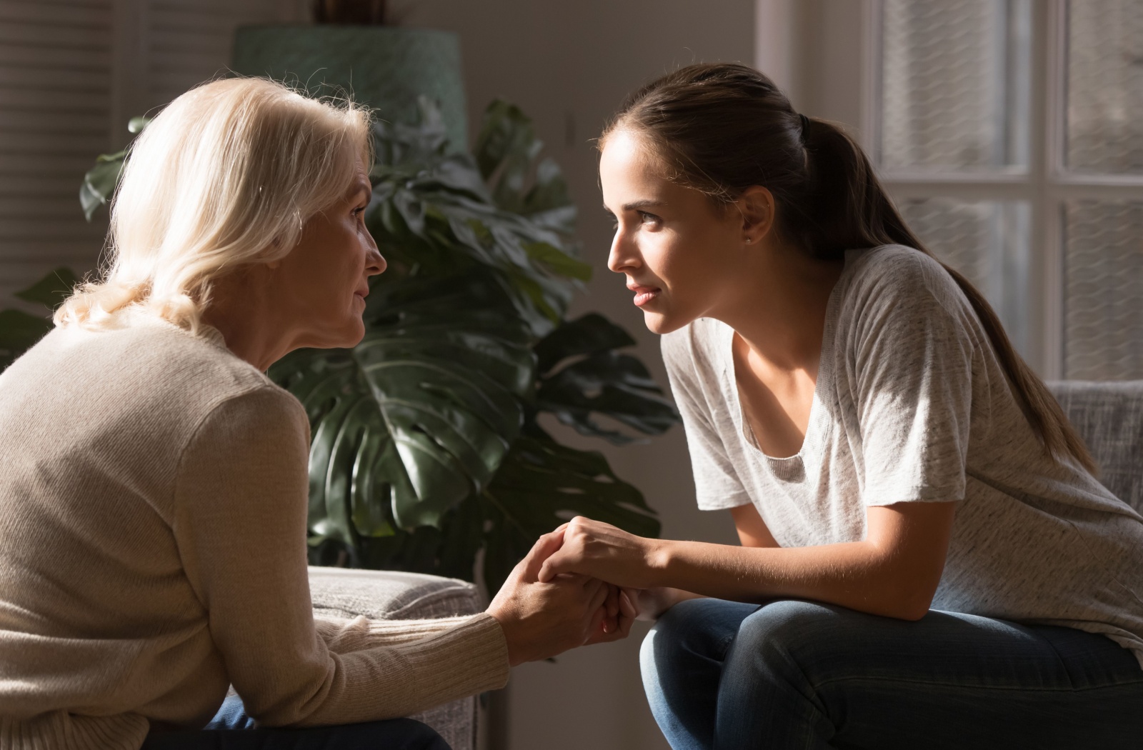 A daughter sitting and holding hands with her older mother, having a heartfelt conversation.