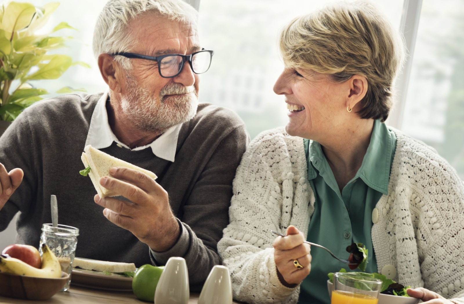 A senior couple enjoying a healthy meal smiling in a sunny indoor setting.
