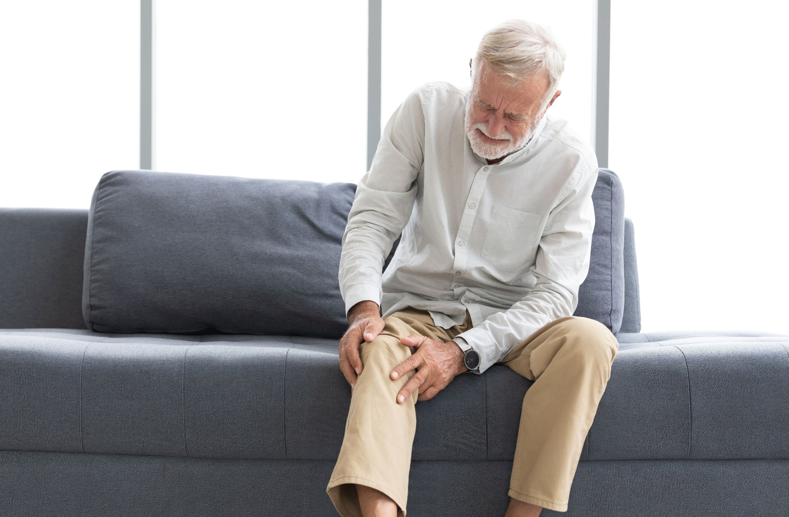 A senior grabs their knee and cringes from pain.
