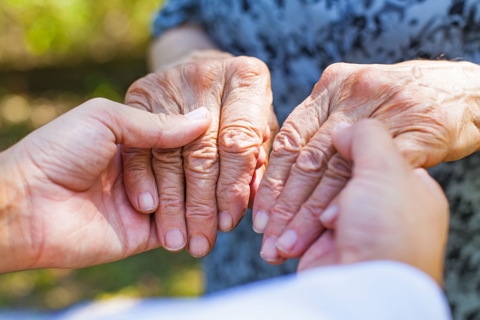 A nurse hands holding hands of senior woman with Parkinson's Disease.