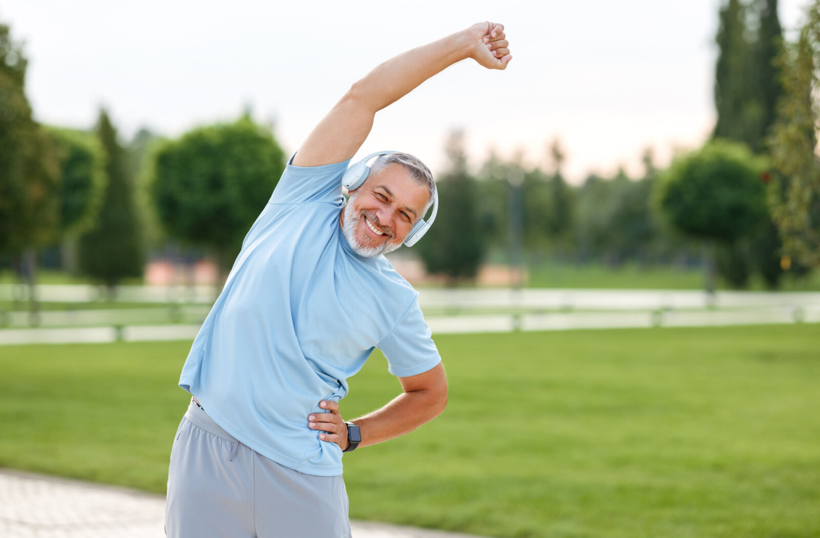 A senior man is doing stretching exercise outdoors.
