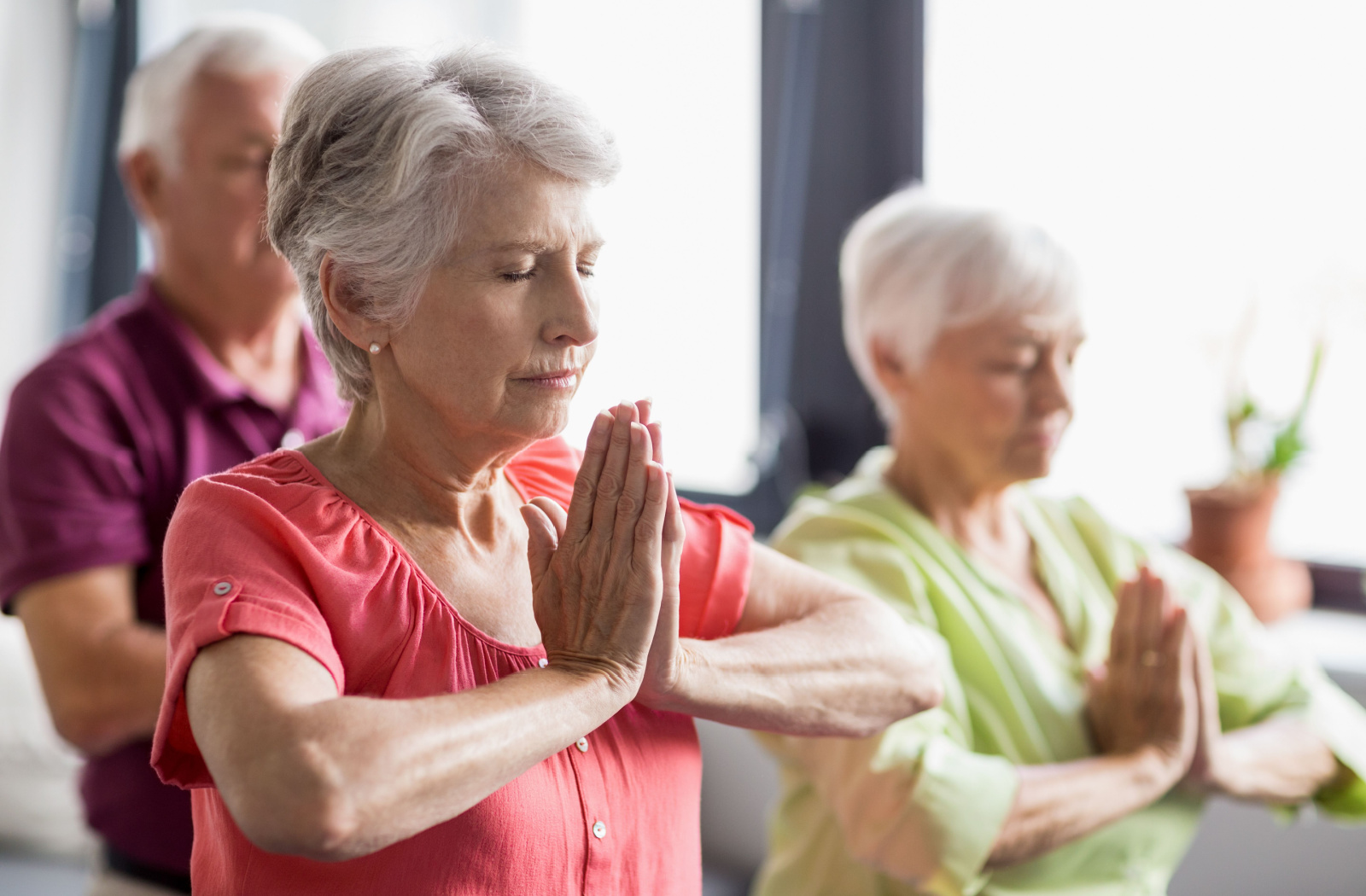 A group of seniors practicing yoga while sitting on mats with their eyes closed.
