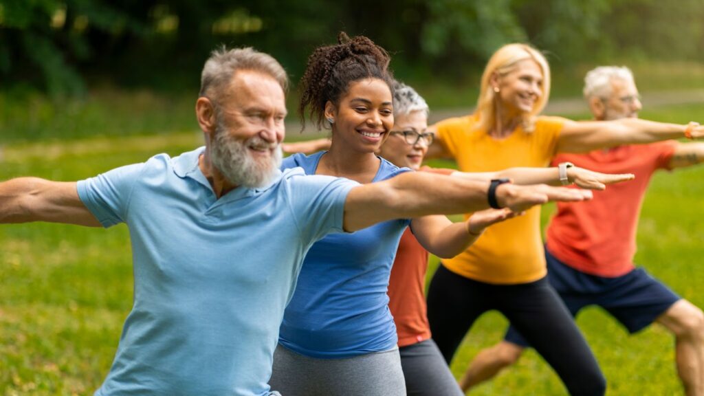 A young woman leads a group of diverse older adults in a yoga exercise in a lush, green park