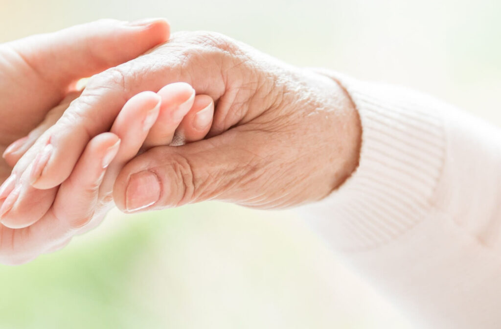 An adult child tenderly holds their senior parent's hand