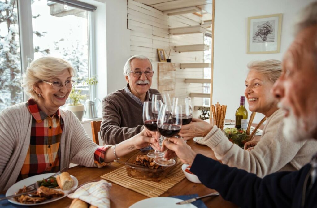 A group of older adults sitting around a table at dinnertime, clinking wine glasses together and happily socializing.