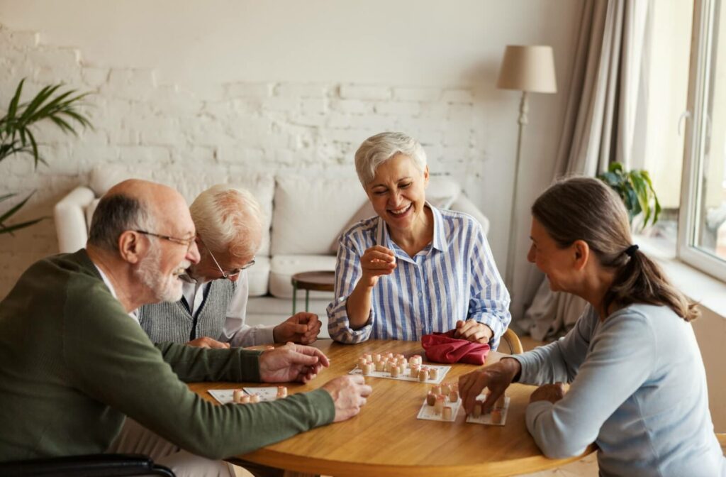 4 older adults sitting around a small table, laughing and playing a board game while socializing in senior living.