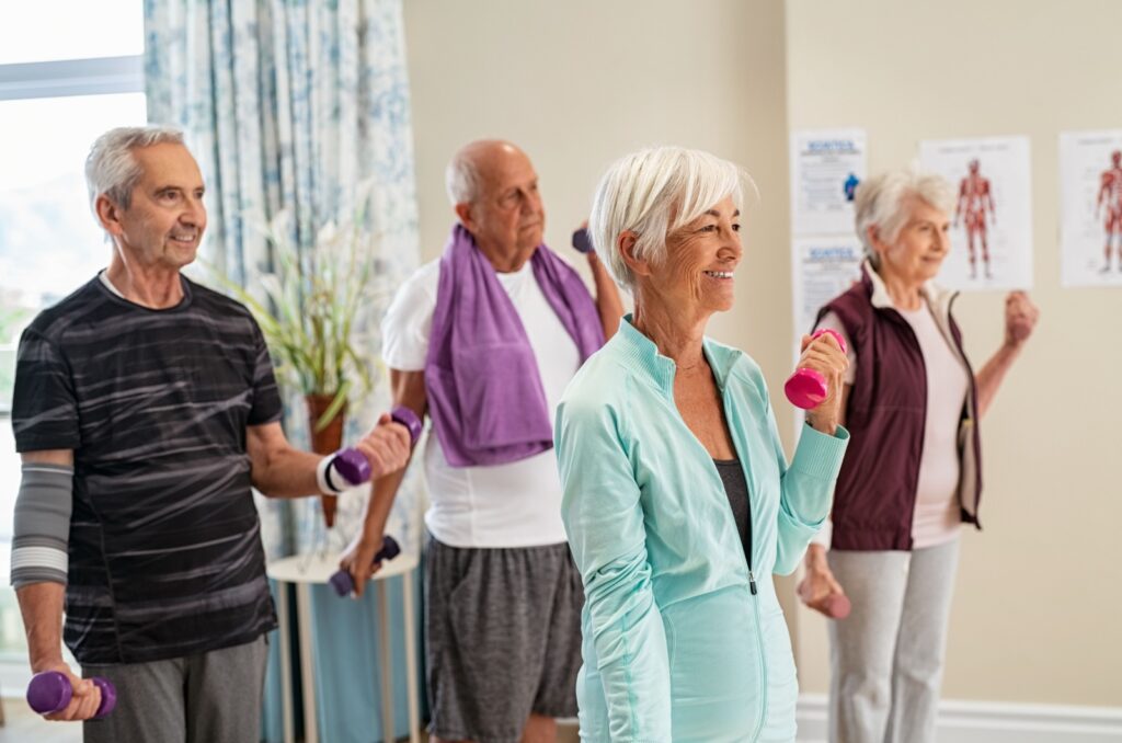 A group of older adults exercising with dumbbells in a fitness class in assisted living.