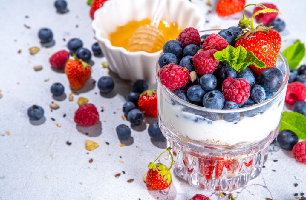 A delicious Greek yogurt and berries parfait beside a small bowl of honey.