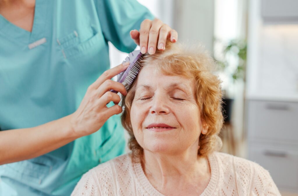 Senior calmly smiling while receiving grooming care from a caregiver in an assisted living community.