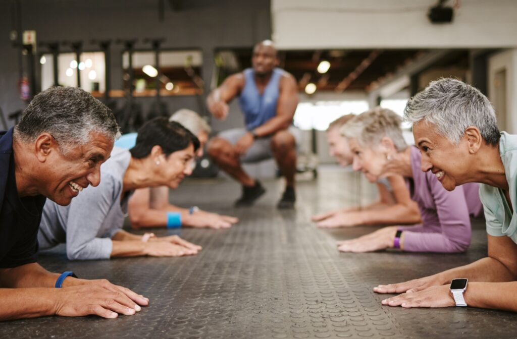 A group of seniors taking a fitness class giggle while performing planks to aid in strengthening their cores.