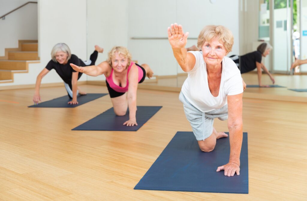 Three seniors use yoga mats in an open studio space to perform opposite arm and leg raises to promote core strength.