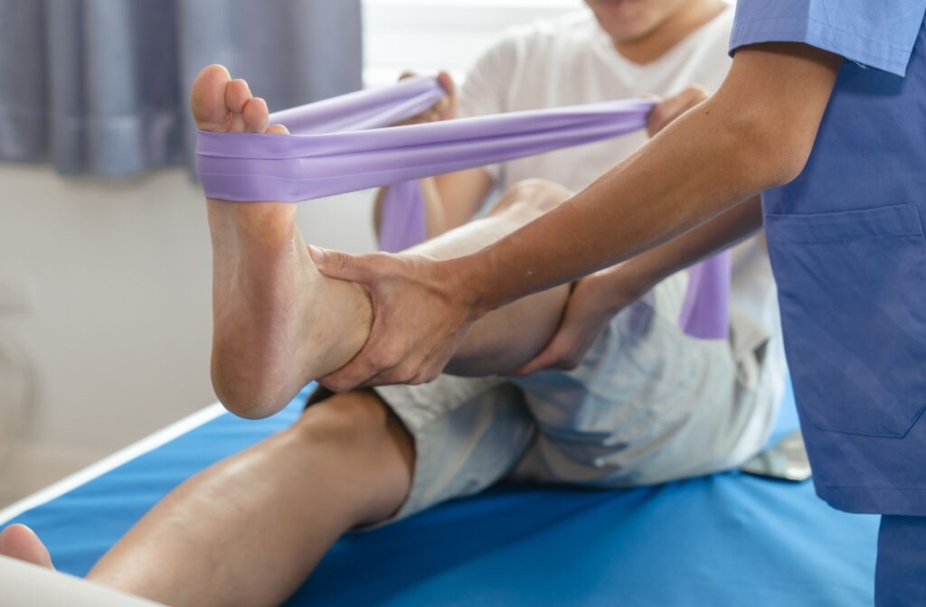 A senior using a resistance band to stretch their ankle, with the support and guidance of a nurse.