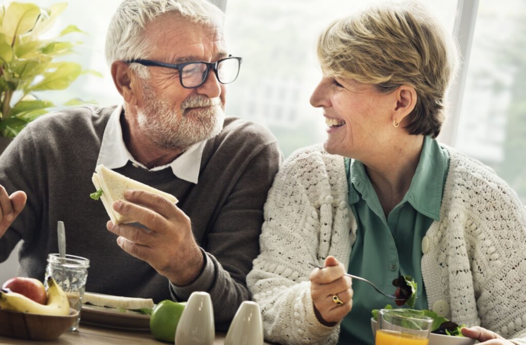 A senior couple enjoying a healthy meal smiling in a sunny indoor setting.
