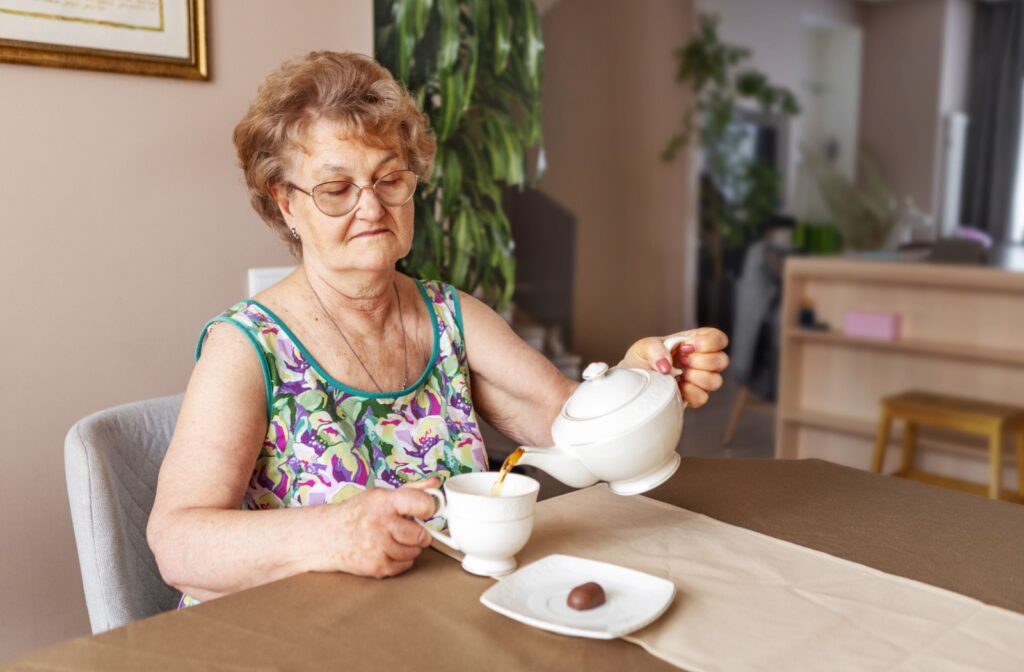 Person pours tea into a cup at a dining table with a plate of chocolate nearby in a cozy indoor setting.