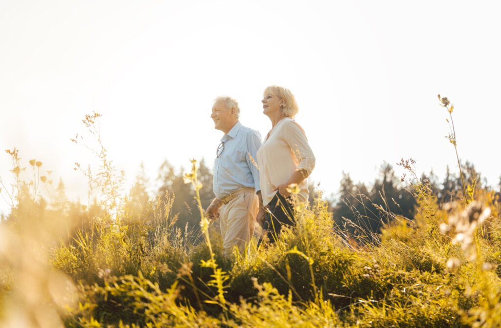 A senior couple enjoy the summertime while walking through a field, getting exercise while spending time together