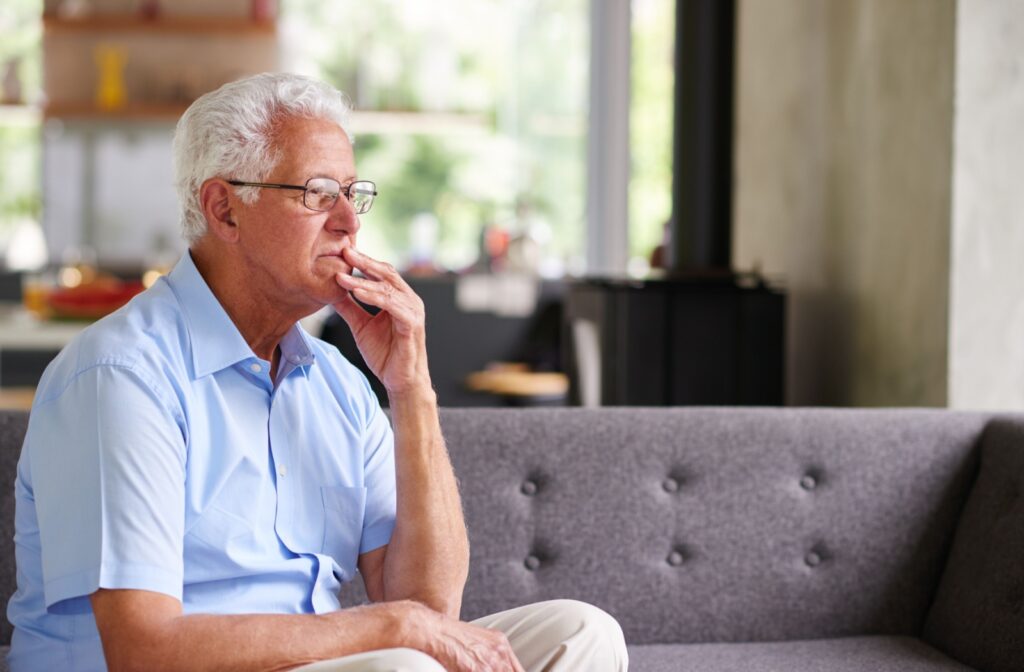 A senior sitting on grey couch in bright home appearing thoughtful about downsizing and moving to independent living