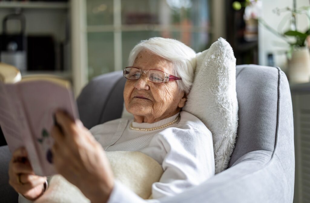 Senior woman with glasses relaxing on armchair reading a book in cozy room