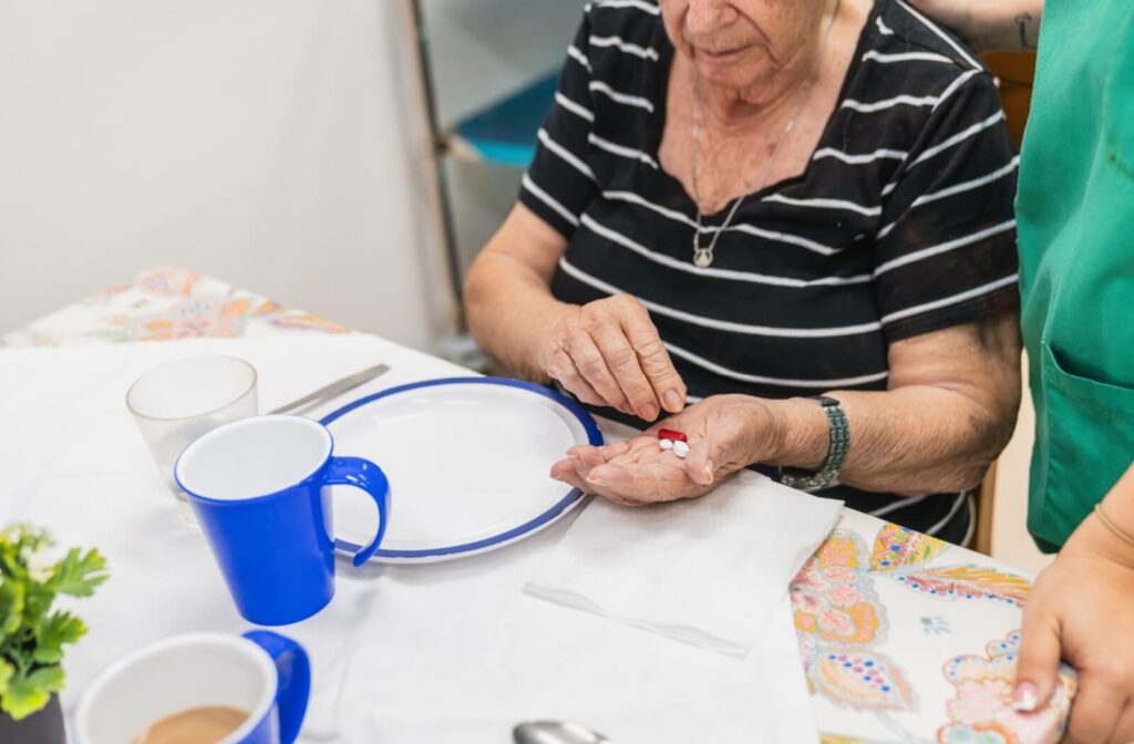 Senior taking daily medications at the table with caregiver’s support during mealtime