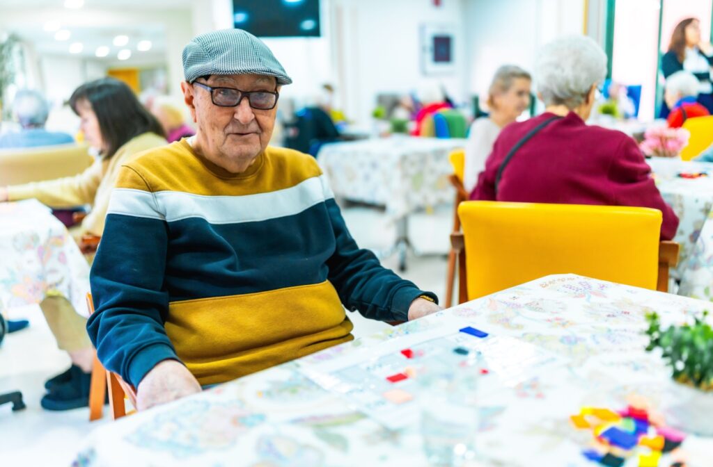 Older adult wearing a cap seated at activity table during group social event in assisted living community